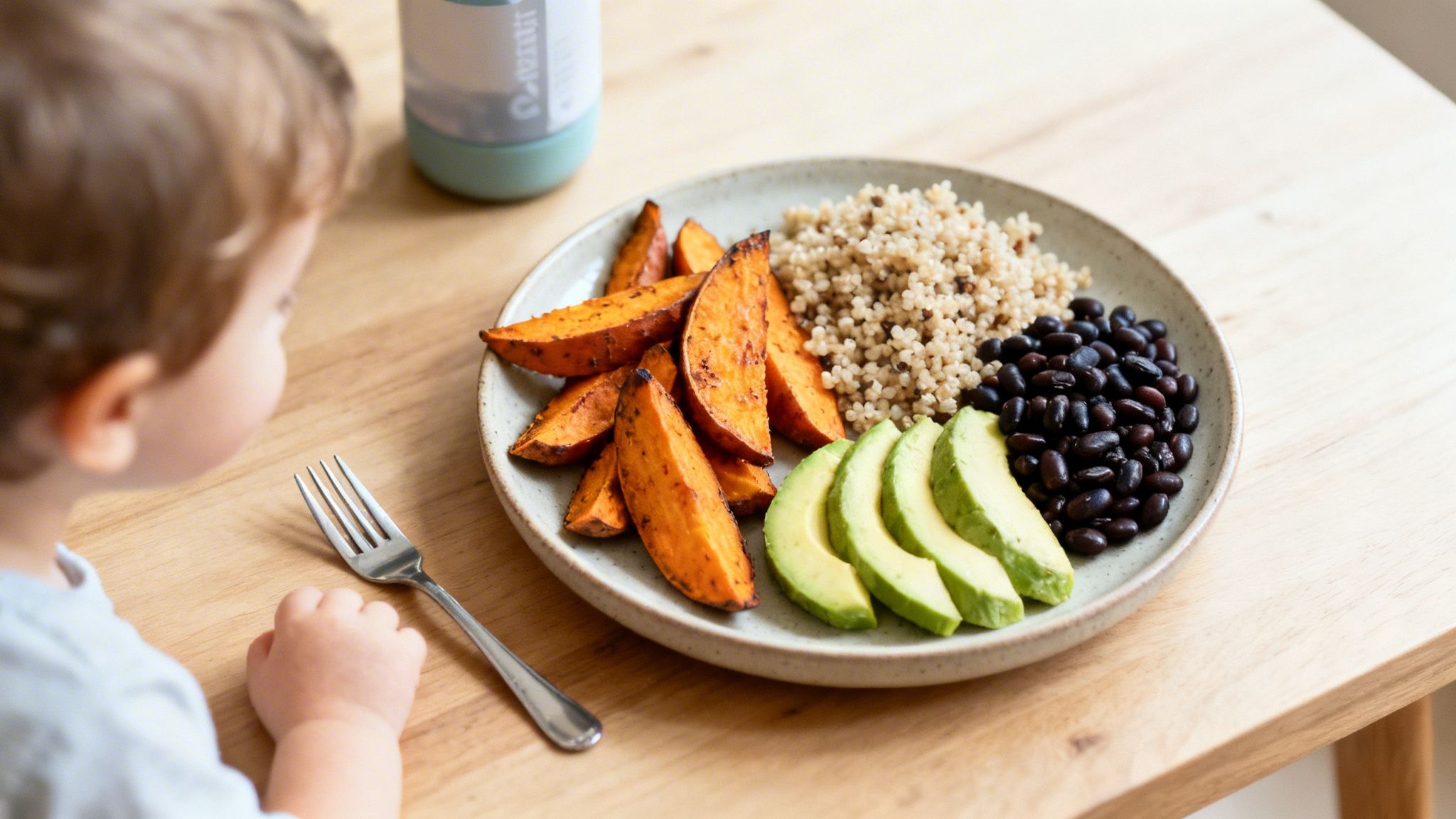Un niño pequeño mira un plato saludable con boniato, quinoa, aguacate y frijoles negros.