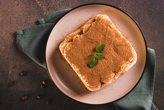 Porción de tiramisú espolvoreada con cacao y decorada con hojas de menta, preparada con crema hecha a base de yemas de huevo pasteurizadas.