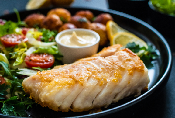 Pedazo de pescadilla frita servida en plato negro