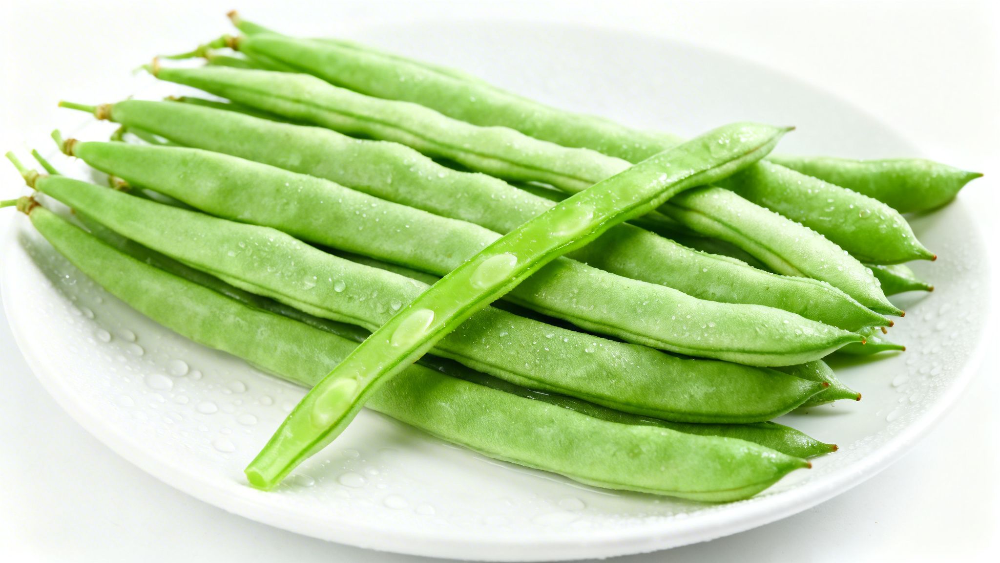 Ejotes verdes frescos con gotas de agua en un plato blanco, uno abierto mostrando las semillas.